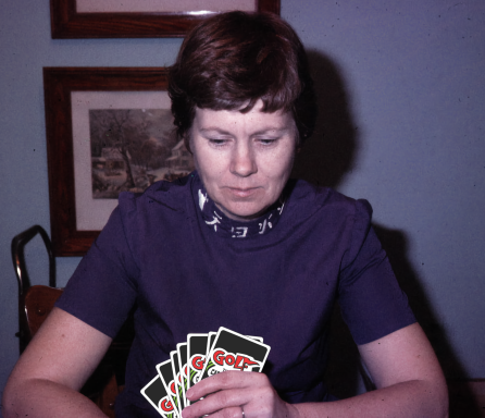 A woman in a purple shirt holding playing cards, focused on the game.