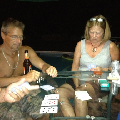 Two people sitting at a table playing cards, with drinks nearby.