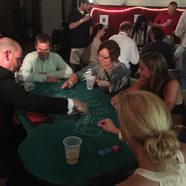 Group of people playing cards around a green table in a lively social setting.