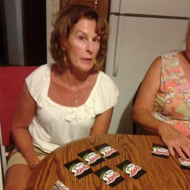 A woman sitting at a table, looking at the camera, with game cards spread out in front.