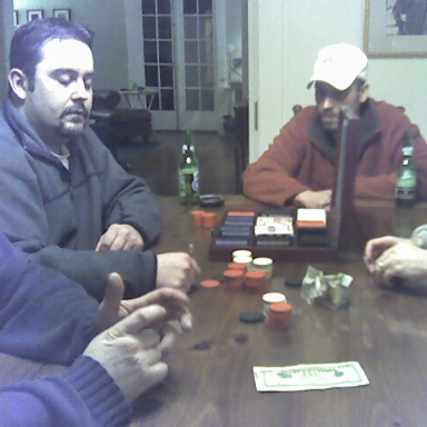 Group of people playing poker at a table, with poker chips and drinks visible.