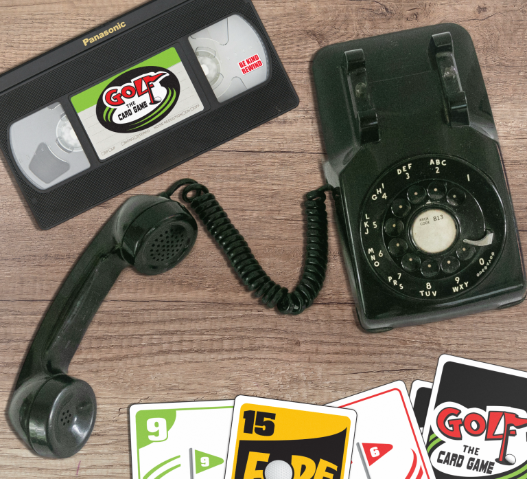 A vintage rotary phone, a VHS tape labeled "Golf the Card Game," and playing cards on a wooden surface.