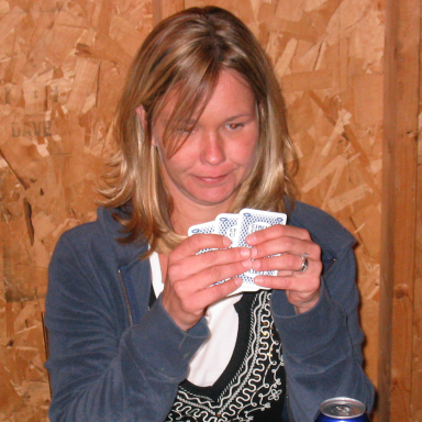 Woman holding playing cards, looking focused, with a wooden wall in the background.