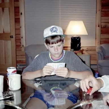 A young child wearing a cap sits at a table, focused on holding cards.