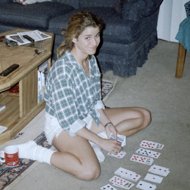 A woman in a plaid shirt sits on the floor playing cards.