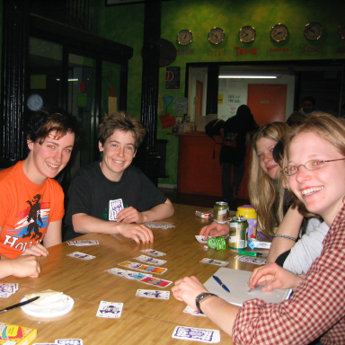 A group of teens sitting around a table playing cards and enjoying snacks.
