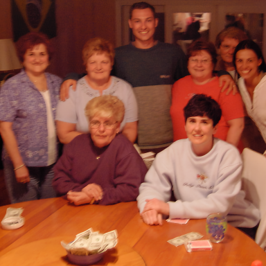 A group of ten people smiling around a table with playing cards and cash.