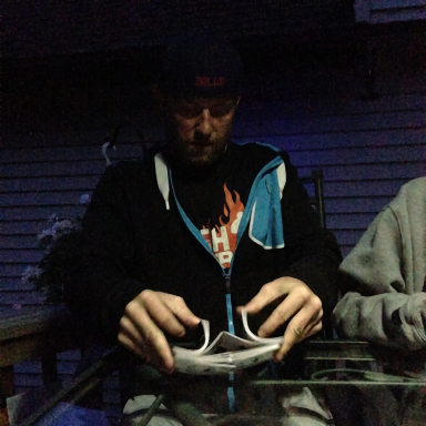 A person sitting at a table, folding a piece of paper, in low light.