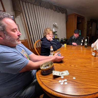 Group of people sitting around a table playing a game, with chips and drinks visible.