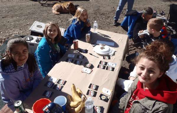 Group of children sitting at a table outdoors, smiling and playing games.