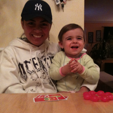 Smiling girl in a baseball cap sits with a small child, both at a table.