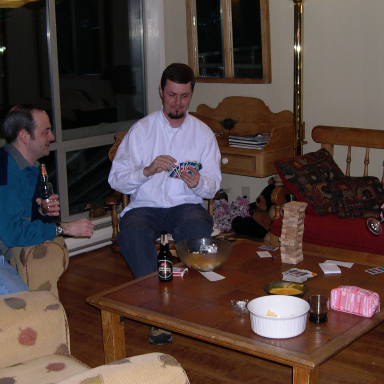 Two men sitting in a living room, playing a game and enjoying drinks.