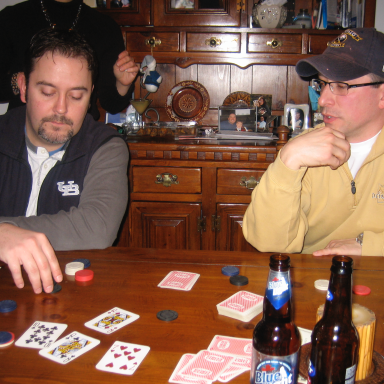 Two men playing cards at a table, with poker chips and beer bottles visible.