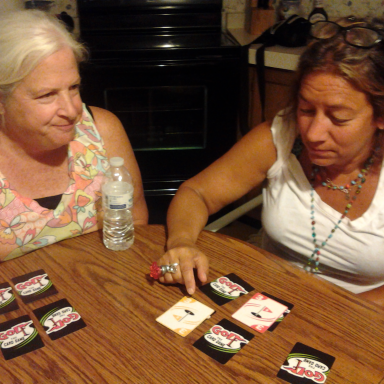 Two women sitting at a table, playing cards and discussing their game. A water bottle is nearby.