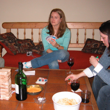 Group of three people playing cards and enjoying snacks and drinks on a sofa.