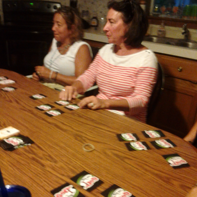 Two women sitting at a table playing cards with several card packets spread out.
